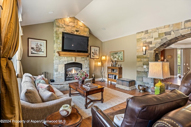 living room featuring hardwood / wood-style flooring, a stone fireplace, and vaulted ceiling