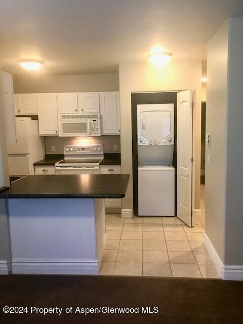 kitchen with white cabinets, white appliances, stacked washer / dryer, and light tile patterned floors