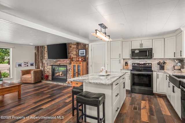 kitchen with backsplash, light stone countertops, open floor plan, a fireplace, and stainless steel appliances