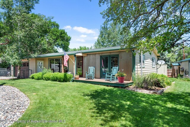 view of front facade featuring french doors, a wooden deck, a front yard, and fence