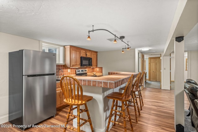 kitchen with tasteful backsplash, light wood-type flooring, a kitchen breakfast bar, appliances with stainless steel finishes, and a peninsula