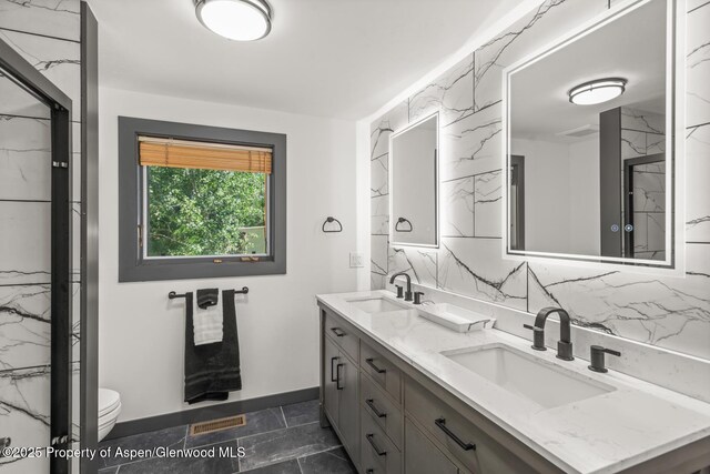 full bath featuring double vanity, toilet, backsplash, and a sink