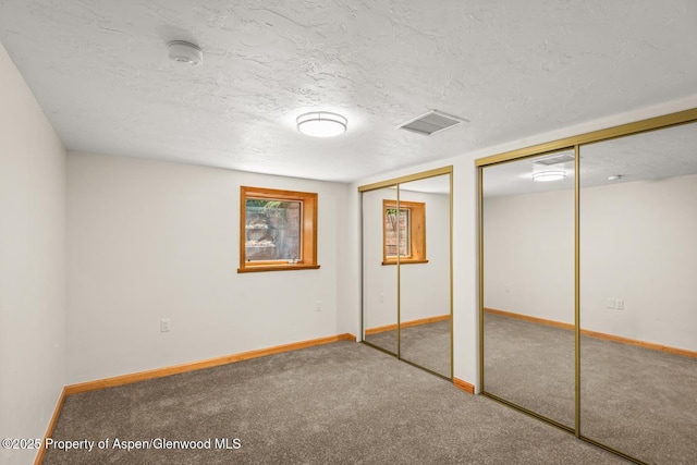 unfurnished bedroom with baseboards, visible vents, a textured ceiling, carpet flooring, and two closets