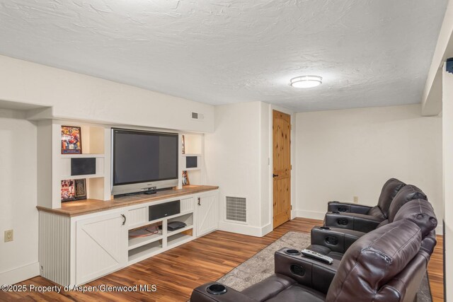 living room with visible vents, baseboards, a textured ceiling, and wood finished floors