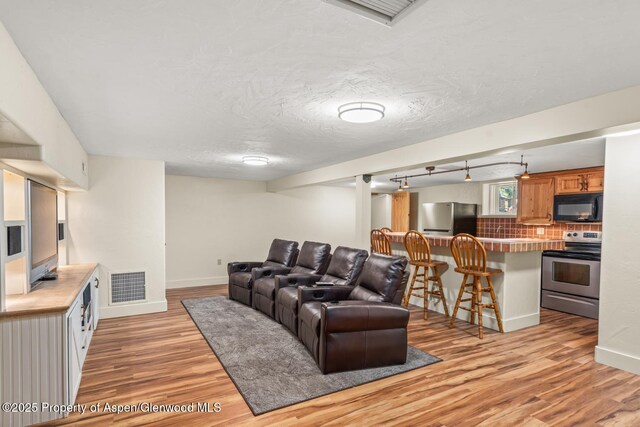 living area with light wood-style flooring, baseboards, visible vents, and a textured ceiling