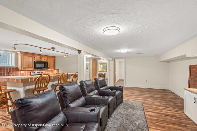 living room featuring track lighting, a textured ceiling, baseboards, and wood finished floors