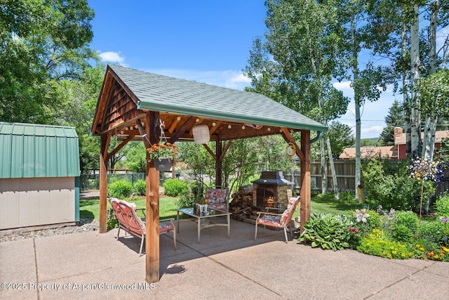 view of patio / terrace featuring a gazebo, a warm lit fireplace, and fence