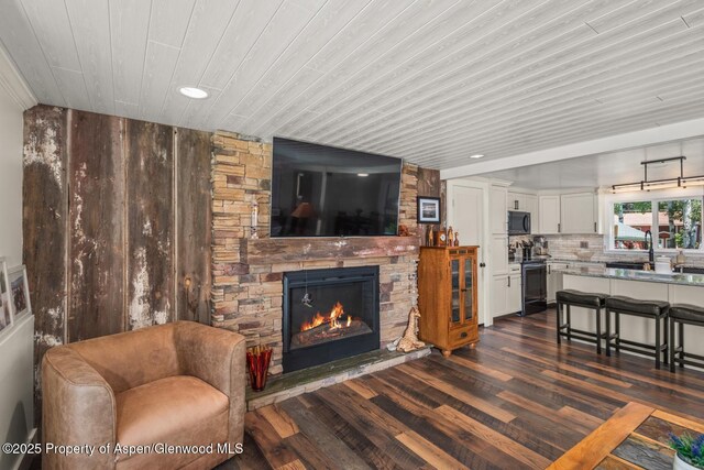 living area featuring dark wood finished floors, a stone fireplace, recessed lighting, and wooden ceiling