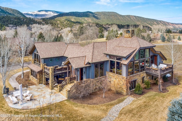 rear view of house featuring a patio area, stone siding, a mountain view, and stairs