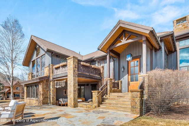 exterior space with a patio area, stone siding, board and batten siding, and a balcony