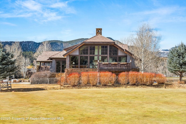 back of house with a yard, a mountain view, and a chimney