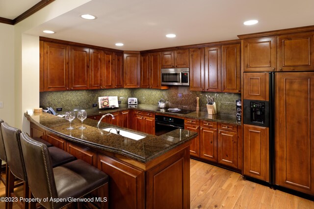 kitchen featuring sink, light hardwood / wood-style flooring, crown molding, a kitchen bar, and black appliances