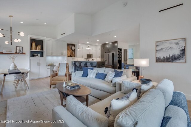 living room with built in shelves, an inviting chandelier, high vaulted ceiling, and light hardwood / wood-style flooring