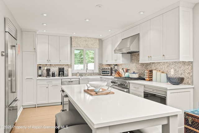 650 S Monarch St Unit 10, Aspen, CO 81612 - kitchen featuring wall chimney range hood, high end appliances, a kitchen bar, light wood finished floors, and light countertops