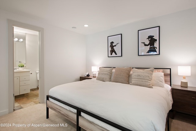 bedroom with ensuite bathroom and light colored carpet