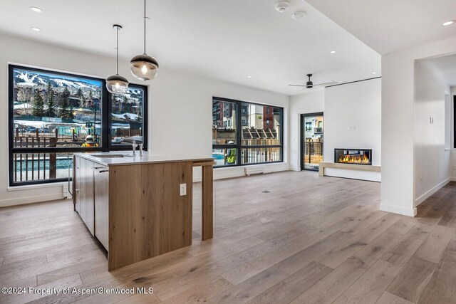 kitchen with sink, ceiling fan, light wood-type flooring, an island with sink, and decorative light fixtures