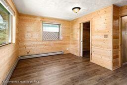 8984 County Road 300, Parachute, CO 81635 - empty room with wood walls, plenty of natural light, dark wood finished floors, and a baseboard heating unit