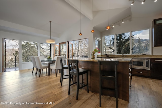 kitchen with light wood-style flooring, a center island, light stone countertops, stainless steel microwave, and a kitchen bar