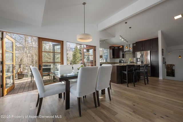 dining area with lofted ceiling with beams and light wood-style flooring