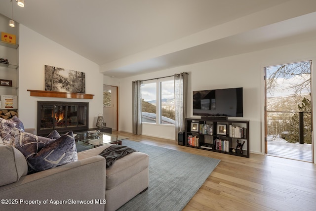 living room with vaulted ceiling, a glass covered fireplace, wood finished floors, and baseboards