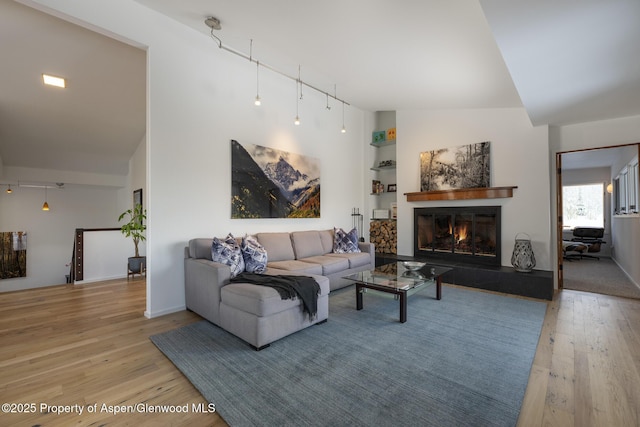 living room featuring light wood-type flooring, a glass covered fireplace, vaulted ceiling, and track lighting