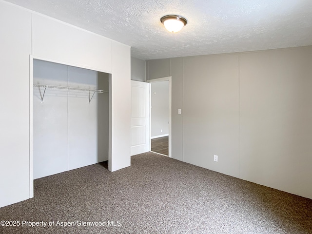 unfurnished bedroom featuring dark colored carpet, a textured ceiling, and a closet