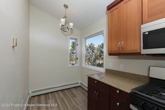 kitchen with lofted ceiling, a baseboard heating unit, gas range oven, light stone counters, and a chandelier