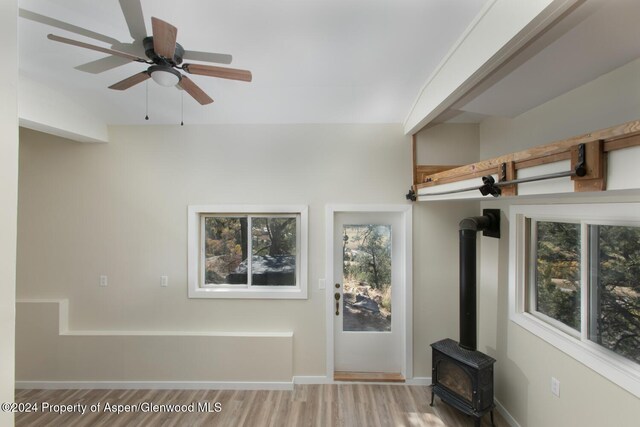 unfurnished living room featuring a wood stove, ceiling fan, and hardwood / wood-style flooring