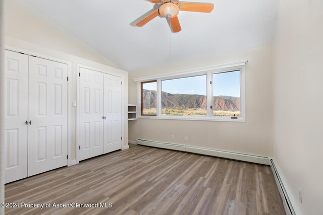 unfurnished bedroom featuring a mountain view, lofted ceiling, baseboard heating, and multiple closets