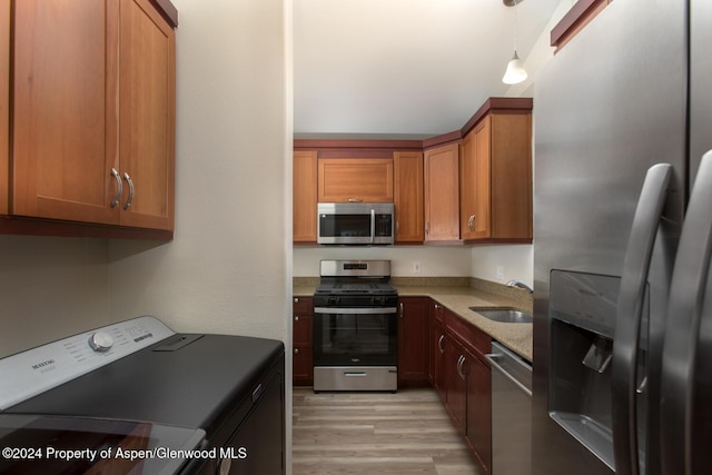 kitchen featuring stainless steel appliances, sink, light hardwood / wood-style flooring, washer / dryer, and hanging light fixtures