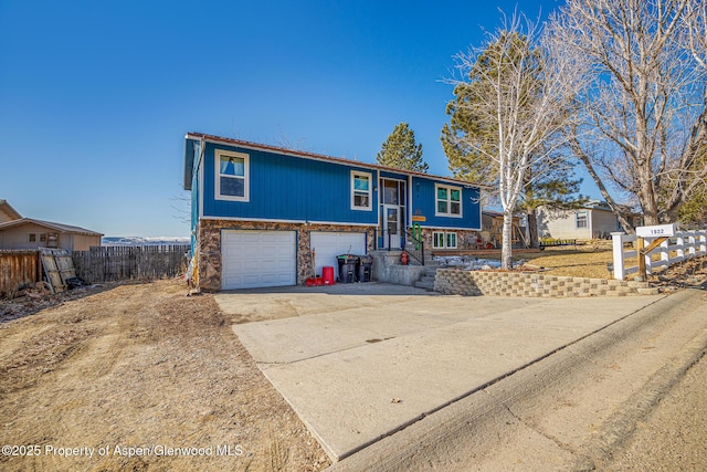 view of front of home with stone siding, an attached garage, concrete driveway, and fence