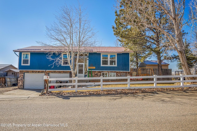 view of front of property featuring an attached garage, concrete driveway, stone siding, a fenced front yard, and metal roof