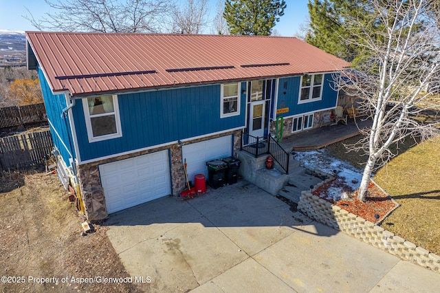 raised ranch with metal roof, stone siding, concrete driveway, and fence