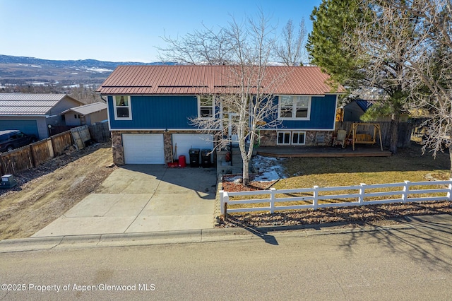 split foyer home with a fenced front yard, stone siding, metal roof, and concrete driveway