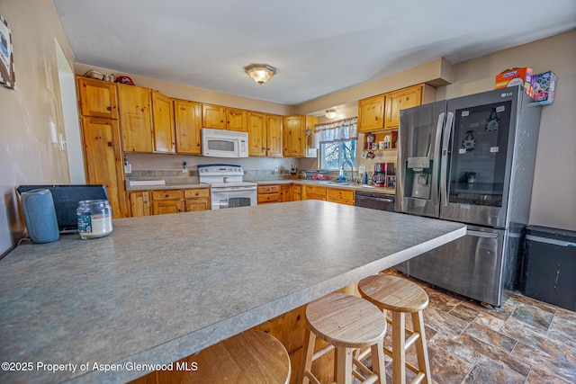 kitchen featuring stone finish flooring, light countertops, a peninsula, a kitchen breakfast bar, and stainless steel appliances