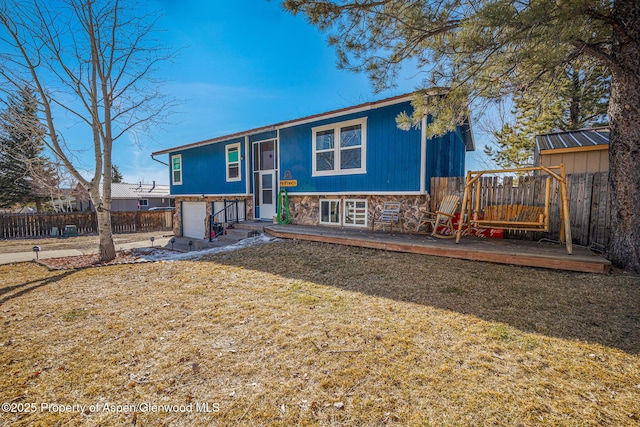 split foyer home with fence, a front lawn, a garage, stone siding, and a deck