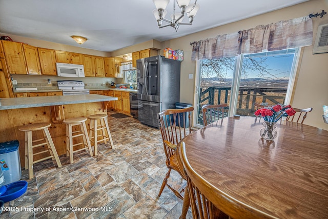 kitchen featuring stone finish flooring, light countertops, a kitchen breakfast bar, a notable chandelier, and white appliances