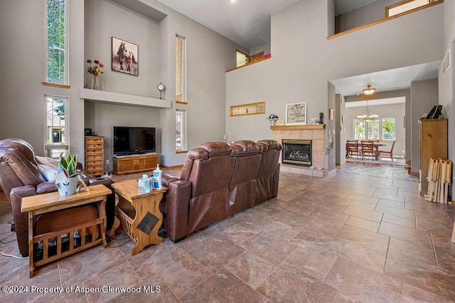 living room with baseboards, a tiled fireplace, a chandelier, a high ceiling, and stone finish floor