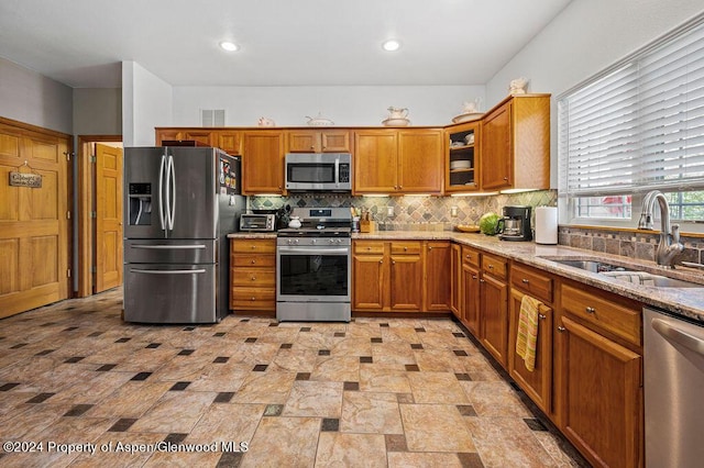 kitchen featuring visible vents, a sink, light stone counters, appliances with stainless steel finishes, and brown cabinetry