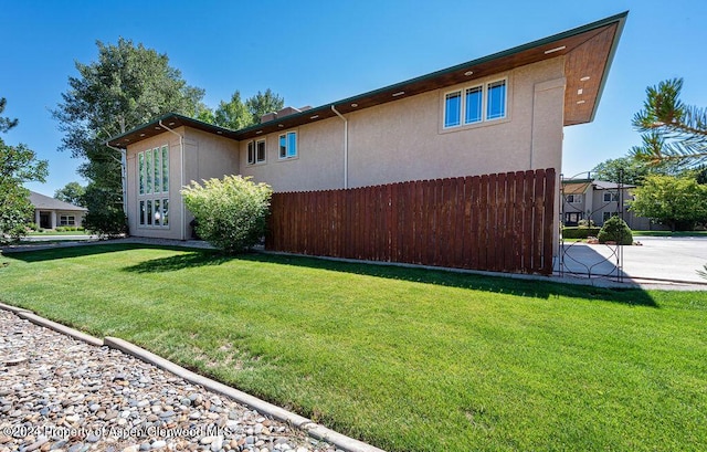 view of property exterior with stucco siding, a yard, and fence