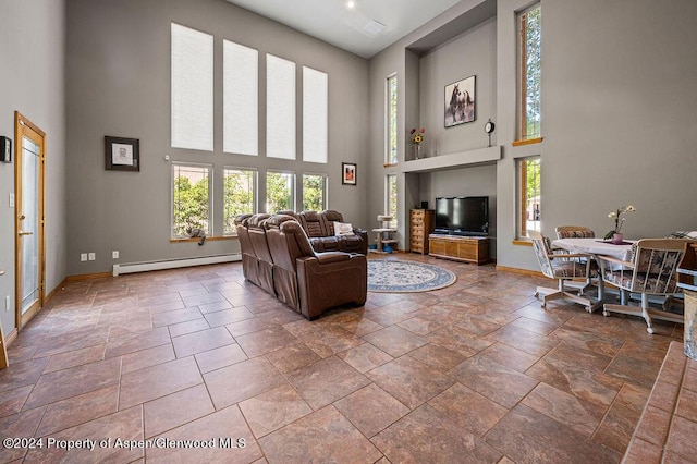 living room featuring a wealth of natural light, baseboard heating, baseboards, and a towering ceiling