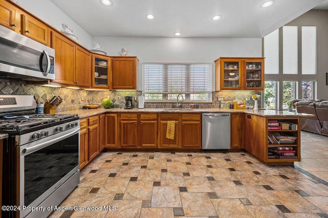 kitchen featuring backsplash, brown cabinets, appliances with stainless steel finishes, a peninsula, and a sink