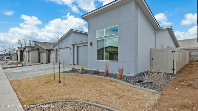 view of front facade with an attached garage, driveway, fence, and stucco siding