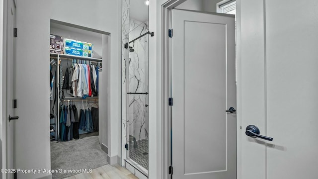 full bath featuring a marble finish shower, a walk in closet, and wood finished floors