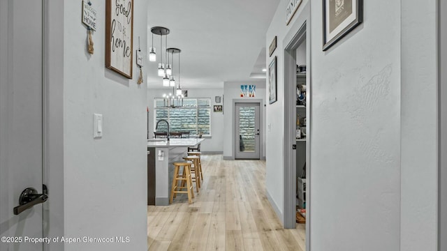 corridor featuring a sink, light wood-style flooring, and baseboards