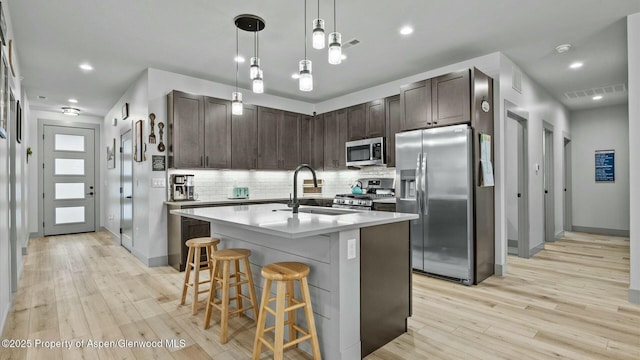 kitchen with dark brown cabinetry, stainless steel appliances, a sink, visible vents, and light wood-type flooring