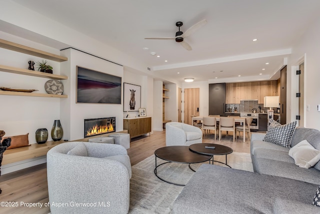 living room featuring a ceiling fan, visible vents, light wood finished floors, recessed lighting, and a glass covered fireplace