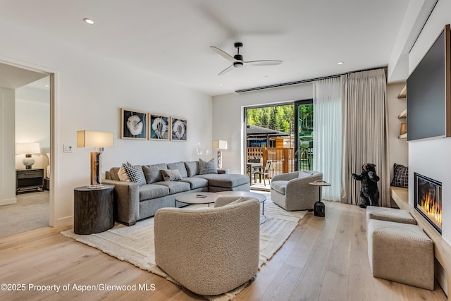 living area featuring light wood finished floors, a glass covered fireplace, recessed lighting, and a ceiling fan