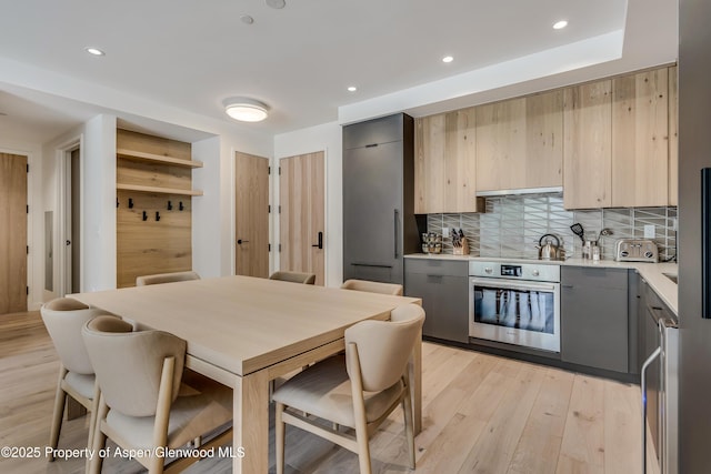 kitchen featuring light wood finished floors, backsplash, oven, light countertops, and gray cabinets