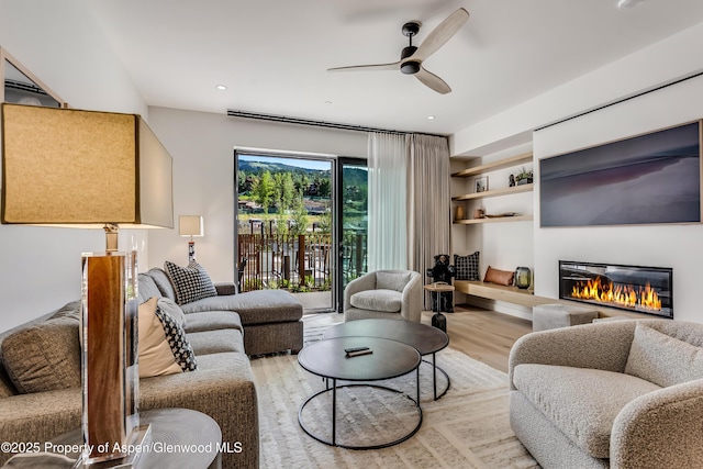 living area with a glass covered fireplace, wood finished floors, recessed lighting, and a ceiling fan